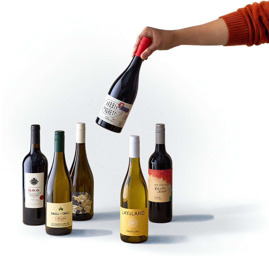 Man's arm holding a wine bottle in the air and placing it among five other upright wine bottles.